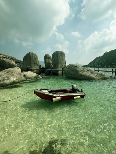 Wooden boat floating in clear turquoise water off the coast of Koh Tao, Thailand, surrounded by coral reefs and tropical scenery
